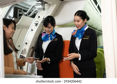 Two young beautiful Asian female flight attendants in suit uniform standing at the airplane entrance smiled friendly checking the Asian female passenger's boarding pass and welcoming her to the flight