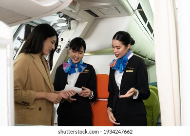 Two Young Beautiful Asian Female Flight Attendants In Suit Uniform Standing At The Airplane Entrance Smiled Friendly Checking The Asian Female Passenger's Boarding Pass And Welcoming Her To The Flight