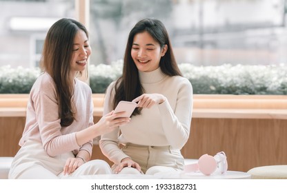 Two young beautiful asian woman is using mobile phone and talking while sitting in coffee shop. Technology and Lifestyle Concept.