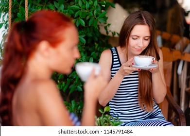 two young beautiful girls drink coffee in an open summer cafe , one of them enjoys the aroma, a warm summer day - Shutterstock ID 1145791484