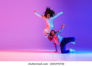 Two young beautiful girls making hip  hop tricks dancing gradient pink purple neon background  Sport achievement  expression  Concept dance  youth  hobby  dynamics  movement  action  ad