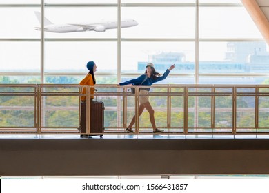 Two young beautiful girls with suitcases are ready for traveling. Young friends are running along terminal hall with suitcases and airplane on background. Do not want to be late. Copy space