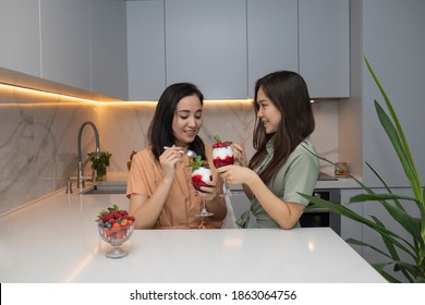 Two young beautiful happy asian girls enjoy berry yogurt dessert while chatting in the kitchen.  - Powered by Shutterstock