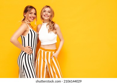 Two Young Beautiful Smiling Brunette Hipster Female In Trendy Summer Clothes. Sexy Carefree Women Posing Near Yellow Wall In Studio. Positive Models Having Fun. Cheerful And Happy