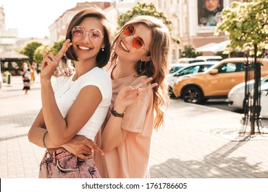 Two young beautiful smiling hipster girls in trendy summer clothes.Sexy carefree women posing on the street background in sunglasses. Positive models having fun and hugging.They going crazy