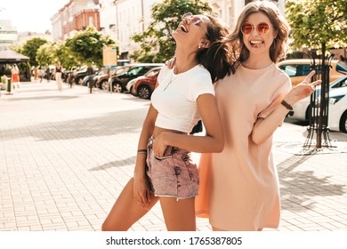 Two young beautiful smiling hipster girls in trendy summer clothes.Sexy carefree women posing on the street background in sunglasses. Positive models having fun and going crazy