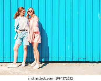 Two young beautiful smiling hipster female in trendy summer clothes and jeans.Sexy carefree women posing in the street near blue wall.Positive pure models having fun at sunset, hugging and going crazy
