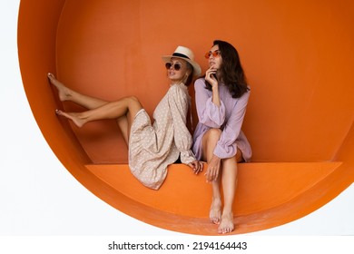 Two young beautiful smiling hipster female in trendy summer sundress.Sexy carefree women posing on the street orange background. Positive models having fun