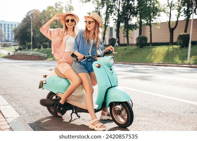 Two young beautiful smiling hipster female in trendy clothes. Carefree women driving retro motorbike on the street background. Positive models having fun, riding classic Italian scooter in Europe city - Powered by Shutterstock