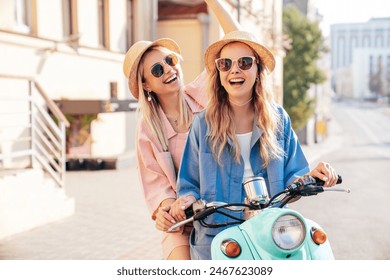 Two young beautiful smiling hipster female in trendy clothes. Carefree women driving retro motorbike on the street background. Positive models having fun, riding classic Italian scooter in Europe city - Powered by Shutterstock