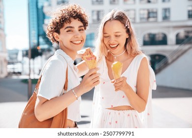 Two young beautiful smiling hipster female in trendy summer clothes. Carefree women posing on street background. Positive models eating tasty ice cream in waffles cone in sunny day, cheerful and happy - Powered by Shutterstock