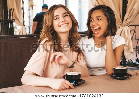 Two young beautiful smiling hipster girls in trendy summer clothes.Carefree women chatting in veranda terrace cafe and drinking coffee.Positive models having fun and communicating