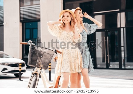 Two young beautiful smiling hipster woman in trendy summer sundress. Carefree women riding retro bicycle. Positive models having fun on bike posing in the park in hats. Best friends outdoors