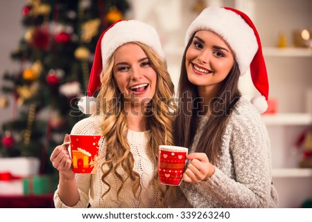 Two young beautiful woman drinks tea, celebrating Christmas at home