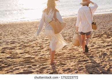 Two Young Beautiful Women Female Friends Going To Have Summer Picnic On A Beach At Sunset. View From Behind.