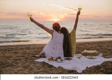 Two young beautiful women female friends having picnic with wine, pizza, cheese and fresh fruits on beach at sunset. - Powered by Shutterstock