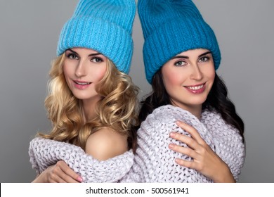 Two Young Beauty Girl In Woolen Hat Isolated On Gray Background. Beautiful Couple Laughing Women's Wrapped Knit Scarf. Curly Hair. Blonde And Brunette