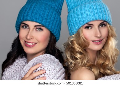 Two Young Beauty Girl In Woolen Hat Isolated On Gray Background. Beautiful Couple Laughing Women's Wrapped Knit Scarf. Curly Hair. Blonde And Brunette