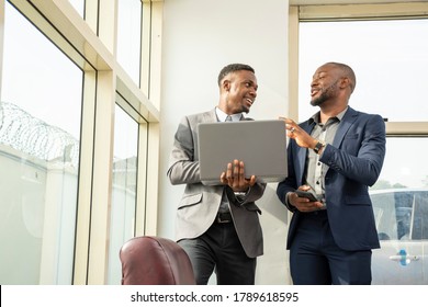 Two Young Black Business Men Standing Together Holding A Laptop, Discussing Business