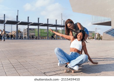 Two Young Black Female Friends Laugh In Amusement Playing With A Skateboard, Concept Of Youth And Friendship, Copy Space For Text