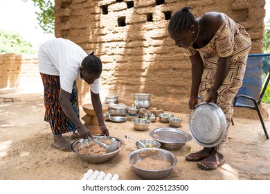 Two Young Black Women Are Preparing A Meal For Their Family Members In Outdoor Air Kitchen In A West African Village