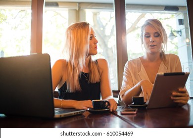 Two Young Blond Female Business Women Having A Business Meeting In A Coffee Shop Over A Cup Of Espresso