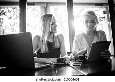 Two Young Blond Female Business Women Having A Business Meeting In A Coffee Shop Over A Cup Of Espresso