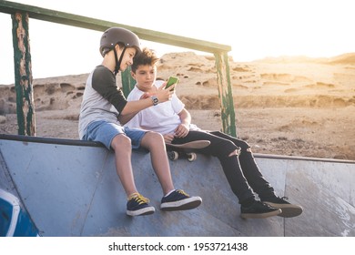 Two young boy using smartphone at the skate park, sitting on an halfpipe ramp. Teenagers communicate with friends with cell phone sharing video from skatepark. Youth, communication, new tech concept.