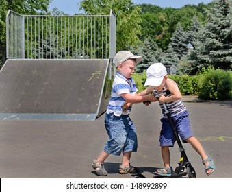 Two Young Boys In Baseball Caps Fighting Over A Scooter In A Skate Park As The One Bullies The Other To Get Off