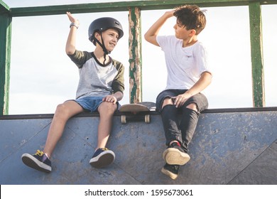 Two young boys hit high five after nice tricks and jumps at the skatepark. Trendy teenagers enjoying free time at the skate park, sitting on half pipe ramp. Youth, togetherness and friendship concept - Powered by Shutterstock