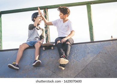 Two young boys hit high five after nice tricks and jumps at the skatepark. Trendy teenagers enjoying free time at the skate park, sitting on half pipe ramp. Youth, togetherness and friendship concept - Powered by Shutterstock