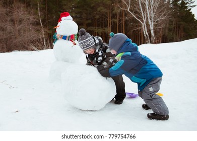 Two Young Boys Make A Snowman On A Winter Day.