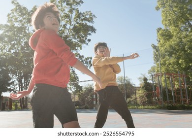 Two young boys are playing a game basketball on a court. One boy is wearing a red hoodie and the other is wearing a yellow hoodie. They are both smiling and enjoying themselves - Powered by Shutterstock