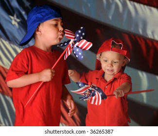 Two Young Brothers Playing With Patriotic Pinwheels In Front Of A Large American Flag.