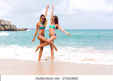 Two Young Brunette And Blonde Best Friends Looking Girls Jumping And Having Fun, Have Sexy Slim Body, Wearing Bikini Sunglasses And Fashion Bright Jewelry, Posing In Front Of Tropical Beach.