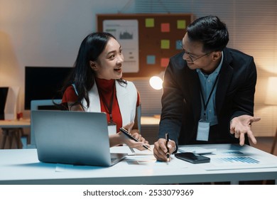 Two young business people reviewing financial data and brainstorming, working late in the office - Powered by Shutterstock