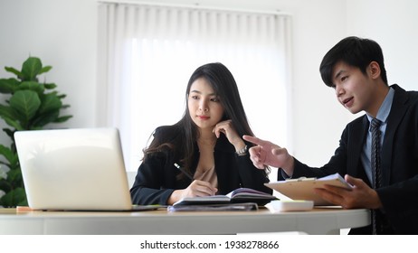 Two young business people using laptop computer searching for business data online in office.