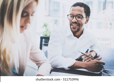 Two Young Business People Working Together In A Modern Office.Black Man Wearing Glasses, Looking At The Businesswoman And Smiling.Woman Discussing With Colleague New Project.Horizontal,blurred