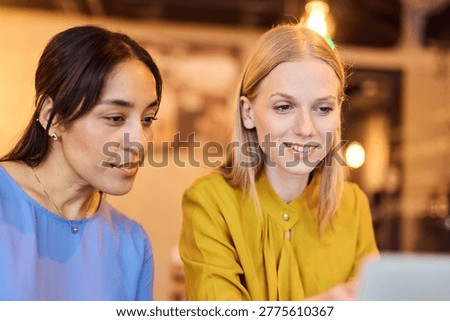 Two young business wmoen using laptop in caffee bar or office