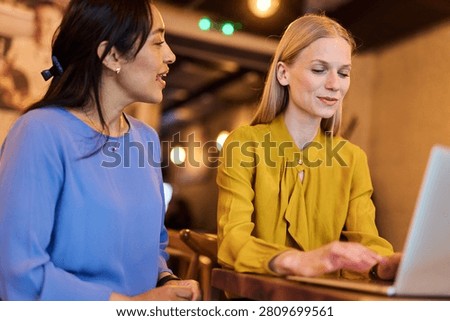 Two young business wmoen using laptop in caffee bar or office