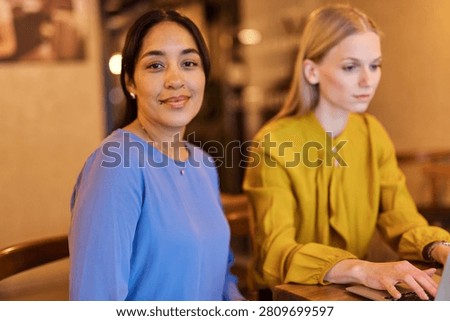 Two young business wmoen using laptop in caffee bar or office
