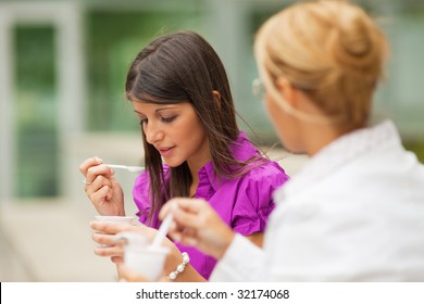 Two Young Business Women Eating Yogurt Outdoors