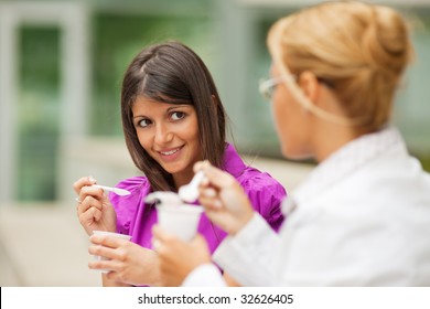 Two Young Business Women Eating Yogurt Outdoors