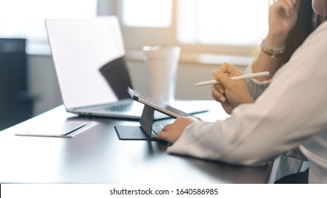 Two Young Business Women Sitting At Table. First Woman Holding Stylus Pen With Digital Tablet Screen. Close Up Side View.