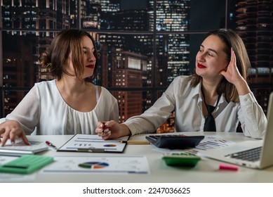 Two young business women working together with buisness graph at ofiice, paperwork concept