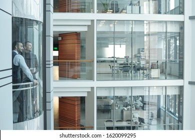 Two young businessmen moving in elevator inside large contemporary business center consisting of many floors