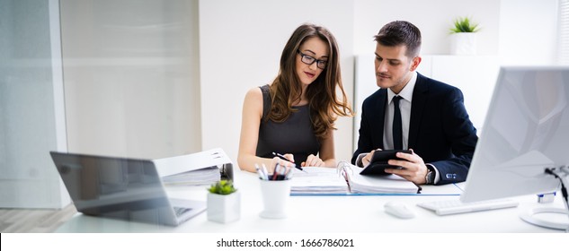Two Young Businesspeople Calculating Invoice With Calculator