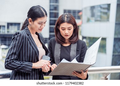 Two Young Businesswomen Looking Into Document File Folder For Analyzing Profit Circulation Or Sale Break Even Point After Marketing. Business Teamwork Employees Of Lifestyle Working Women Concept.