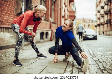 Two young Caucasian female friends stretching and getting ready to run together in the city - Powered by Shutterstock