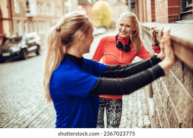 Two young Caucasian female friends stretching and getting ready to run together in the city - Powered by Shutterstock